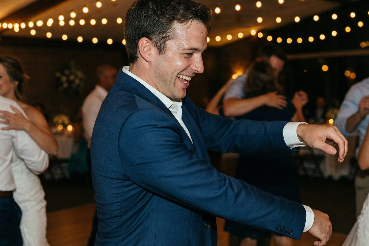 A man dancing in a navy suit jacket at a wedding reception